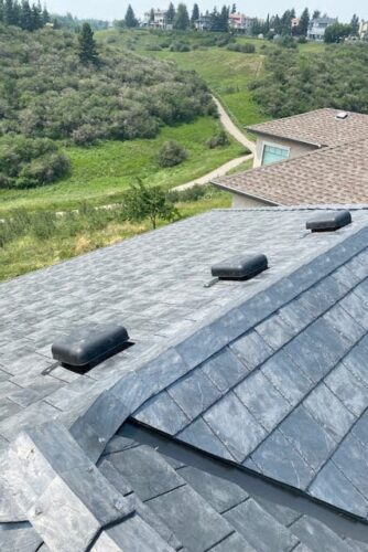 Slate-style roof with low-profile roof vents on a hillside home
